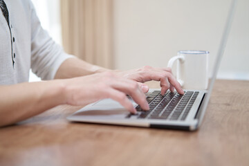自宅でノートパソコンでタイピングをするアジア人男性の手元