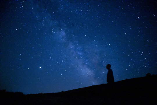 Magical view of a silhouette of a man stargazing the Milky way and the blue night sky