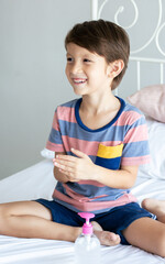 Caucasian cute little boy smiling with happiness and healthy, use alcohol gel washing his hands to protect virus while sitting on bed at home.
