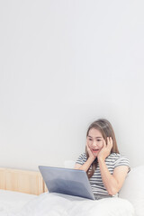 Young Asian woman watching movie with laptop on her bed in white bedroom background.