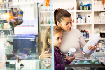 Young attractive woman with little girl looking for aquarium accessories in pet store