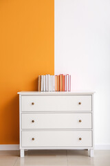 Chest of drawers with books on color background