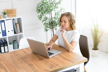 Business woman using laptop sitting near desk white office interior with houseplant looking at camera