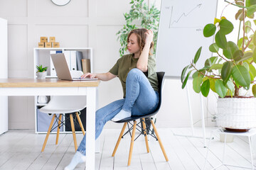 Business woman using laptop sitting desk white modern office interior with houseplant