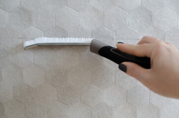 A woman's hand holds a brush for cleaning tile joints.
Narrow brush for hard-to-reach places. Paint brush on an isolated gray background. Cleaning seams and crevices.