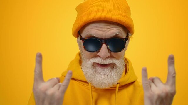 Joyful elderly man posing in studio. Cheerful guy showing rock gesture indoors.
