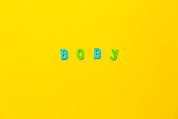 The word Boby made of colored plastic letters with magnets on a yellow background with copy space, text place. Preschool education in a fun color form as a game. A boy name. Banner. English grammar