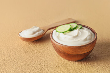Bowl and spoon with tasty sour cream on color background