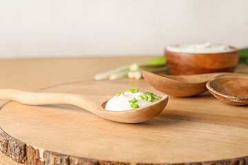 Spoon with tasty sour cream on light wooden background