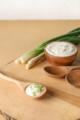 Bowl and spoon with tasty sour cream on light wooden background