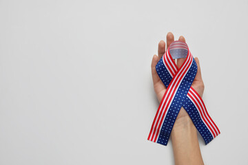 Female hand with ribbon in colors of USA flag on light background