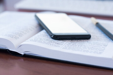 Open book Bible. Phone on the book. White blank screen. Empty table. Office workplace