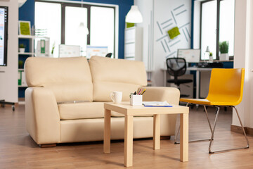 Fototapeta premium Modern business relax zone interior with confortable couch and orange chair. Rest area in company center with small sofa, shot of empty room with modern furniture, white shelves and blue wall.