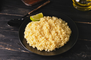 Plate with tasty couscous and lime on dark wooden background