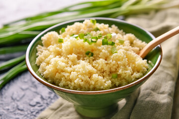 Bowl with tasty couscous and green onion on table, closeup