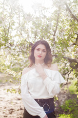 Lovely young girl in a white romantic silk blouse in spring in a blooming cherry garden in sunny weather. Spring and Fashion. Spring blooming gardens