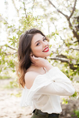 Lovely young girl in a white romantic silk blouse in spring in a blooming cherry garden in sunny weather. Spring and Fashion. Spring blooming gardens