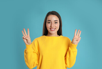 Woman showing number six with her hands on light blue background