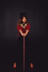 Female magician illusionist circus with wand in theatrical clothes shows and smiles, on black...