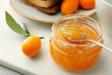 Delicious kumquat jam in glass jar on white board