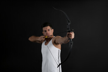 Man with bow and arrow practicing archery on black background