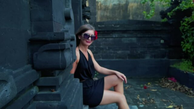 Portrait of attractive woman in black dress and sunglasses sitting in front of shrine. High quality 4k footage
