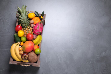 Different tropical fruits in wooden box on grey background, top view. Space for text