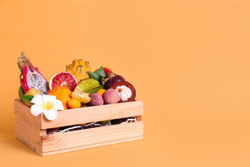 Different tropical fruits in wooden box on yellow background. Space for text