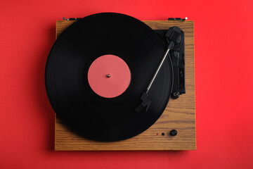 Modern vinyl record player with disc on red background, top view