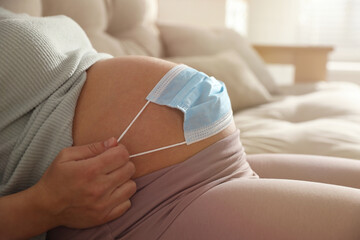Young pregnant woman with medical mask on her belly indoors, closeup