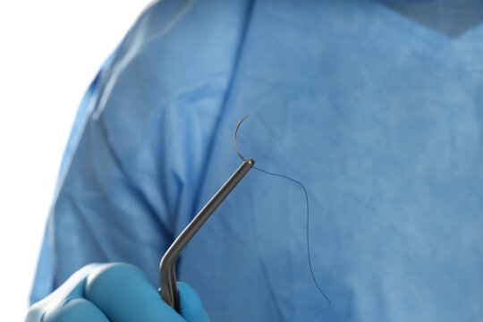 Doctor holding needle with suture thread on white background, closeup. Medical equipment
