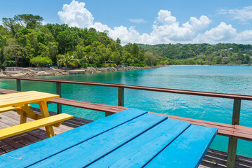 James Bond Beach, Jamaica. A view of the bay, with turquoise waters and green trees in the background. Colorful tables in the foreground.