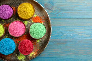 Colorful powder dyes on light blue wooden background, top view with space for text. Holi festival