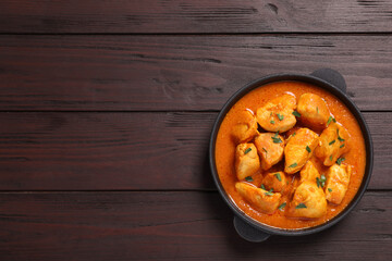 Delicious chicken curry in pan on wooden table, top view. Space for text