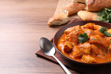 Bowl of delicious chicken curry on wooden table, space for text