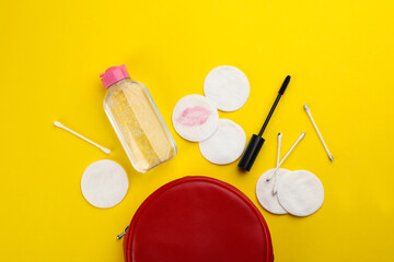 Dirty cotton pads, swabs, mascara and micellar cleansing water on yellow background, flat lay