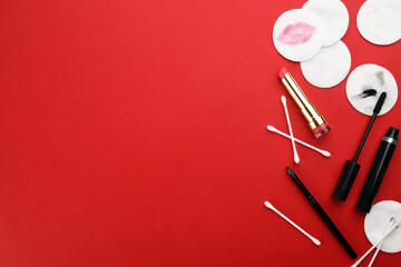 Dirty cotton pads, swabs and cosmetic products on red background, flat lay. Space for text