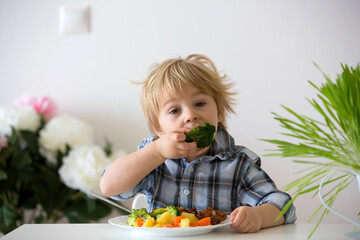 Little toddler child, blond boy, eating boiled vegetables, broccoli, potatoes and carrots with fried chicken meat at home