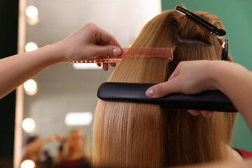 Stylist straightening woman's hair with flat iron in salon