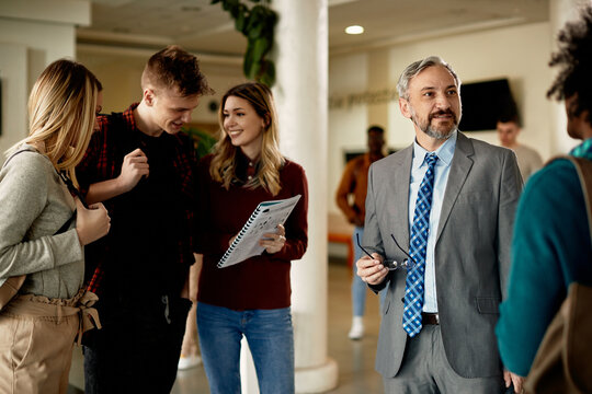 Mature University Professor Talking To His Students In A Hallway.