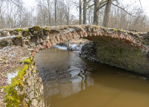 a continuous boulder stone bridge with a brick used for masonry, early spring, bare trees, snow plan on the ground, Stone arch bridge over the river Kuja, Madona, Latvia