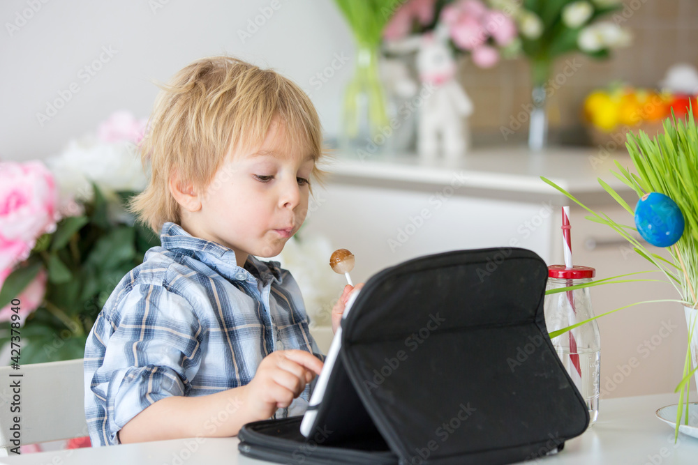 Poster Little toddler child, blond boy, licking lollipop while watching movie on tablet