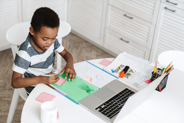 Black boy using laptop and drawing while sitting at home