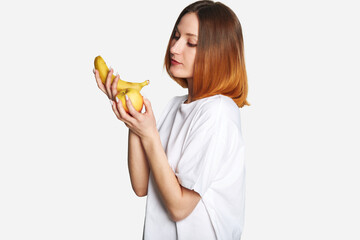 Woman on a diet - eat healthy, fresh fruits. Woman in white t-shirt holding a ripe apple and a banana on gray background copy space