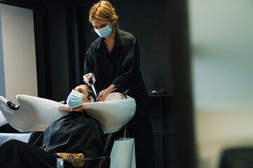 Obraz premium Woman washing her client's hair while doing hairstyle in beauty salon