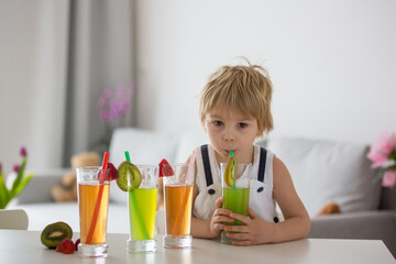 Cute toddler child, blond boy, drinking freshly made fruit juice at home