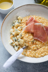 Plate of pumpkin risotto with prosciutto ham and gorgonzola cheese, vertical shot, closeup