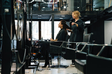 Fototapeta na wymiar Young blonde woman doing hairstyle for her client in beauty salon