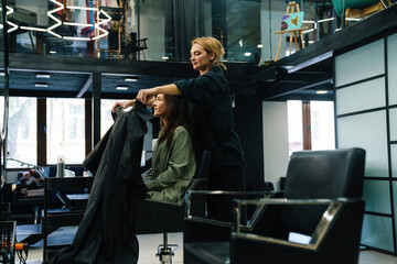 Young blonde woman doing hairstyle for her client in beauty salon