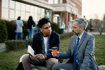African American student consulting with his teacher about lecture in a book at campus.